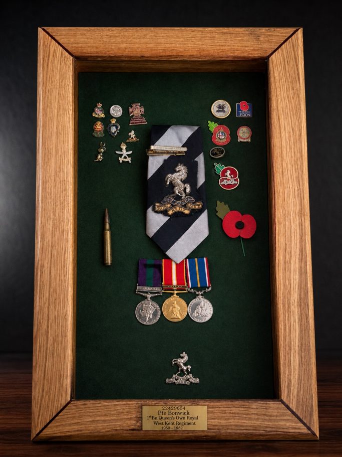 A framed display of medals, badges, and a poppy on a green background.